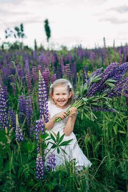 Cute baby in white dress in lupine field