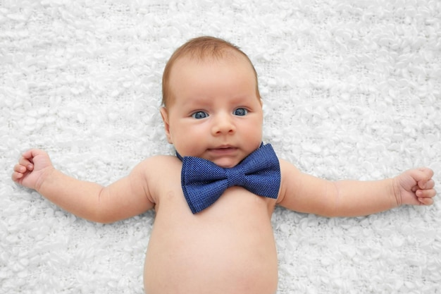 Cute baby with bow tie lying on white bedspread