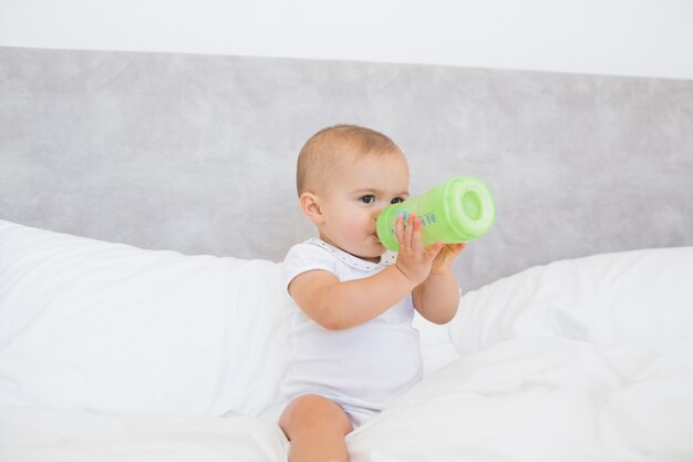 Cute baby with milk bottle sitting on bed