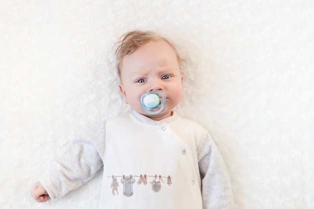 Cute baby with pacifier on a white blanket