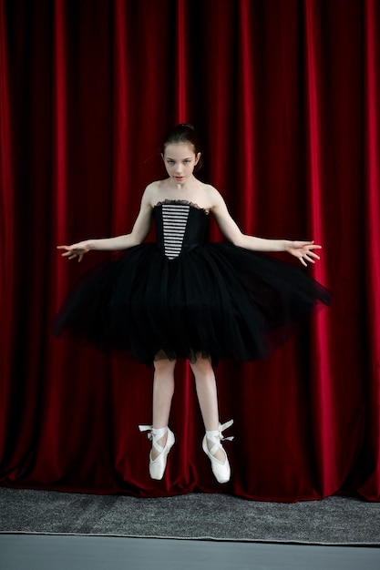 A cute ballerina girl in a black dress on a red background art
dance beauty