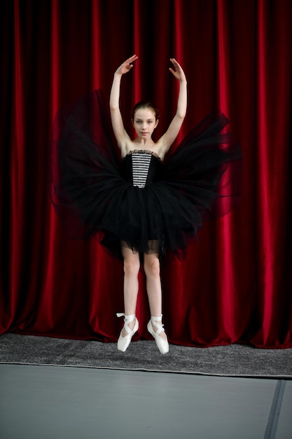 A cute ballerina girl in a black dress on a red background art\
dance beauty