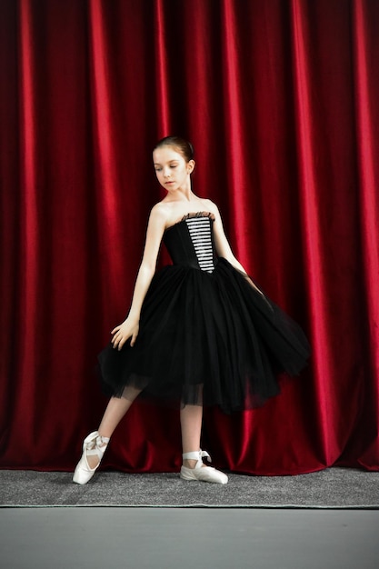 A cute ballerina girl in a black dress on a red background.\
art. dance. beauty.