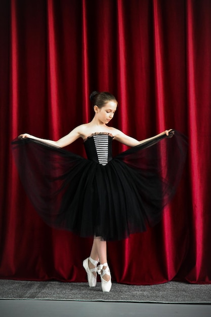 A cute ballerina girl in a black dress on a red background art\
dance beauty