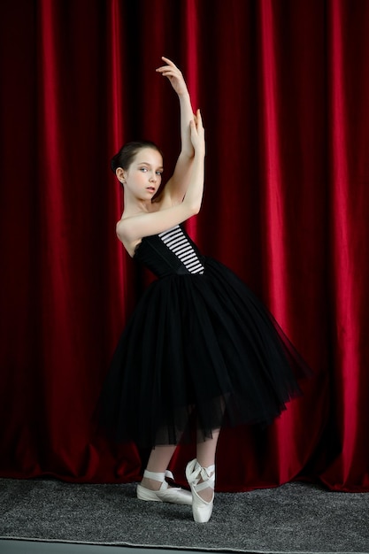 A cute ballerina girl in a black dress on a red background art
dance beauty