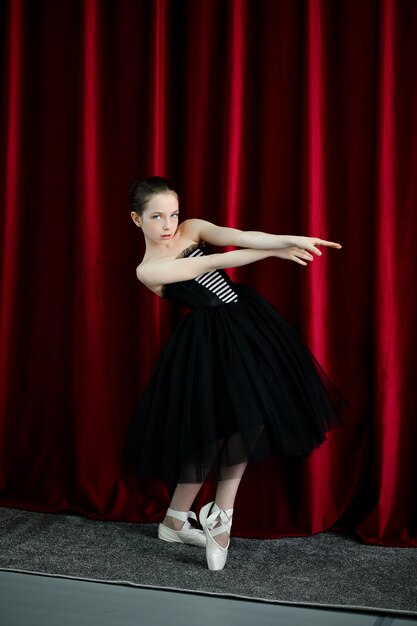 A cute ballerina girl in a black dress on a red background art\
dance beauty