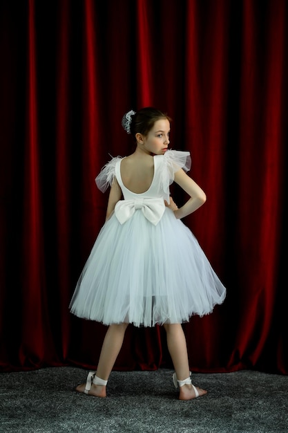 A cute ballerina girl in a white dress on a red background art\
dance beauty