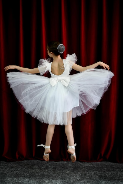 A cute ballerina girl in a white dress on a red background art\
dance beauty