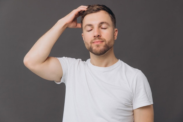 cute bearded man massaging his scalp on gray background in studio beauty and care concept