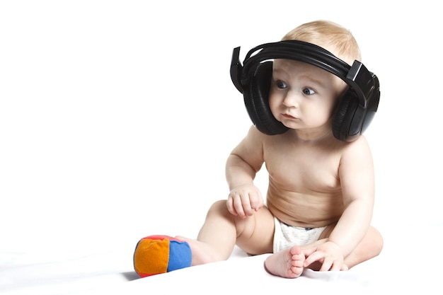 Cute beautiful baby smiles and listens to music in black headphones on a white background Children education