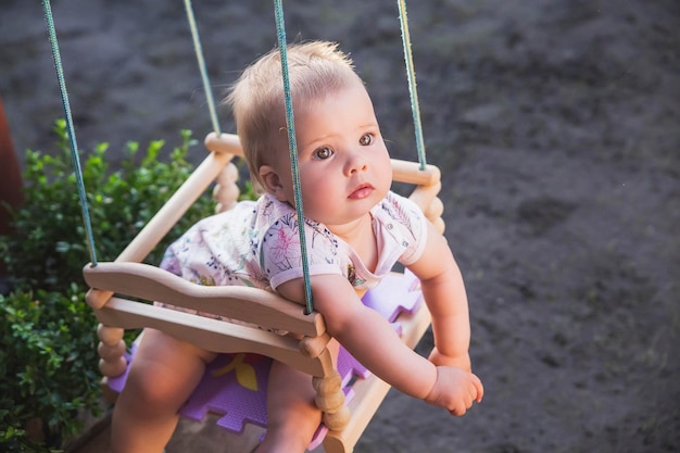 cute beautiful baby swinging in the yard on a children's swing sticking