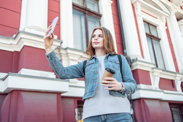 街中でスマートフォンで自撮りをするかわいい美しい白人女性