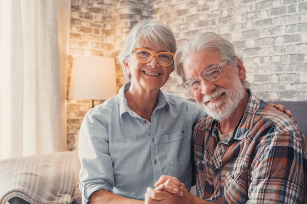 Cute and beautiful couple of old people smiling and looking at the camera having fun at home together Portrait of seniors wearing eyeglasses sitting on sofa enjoying and relaxingxA