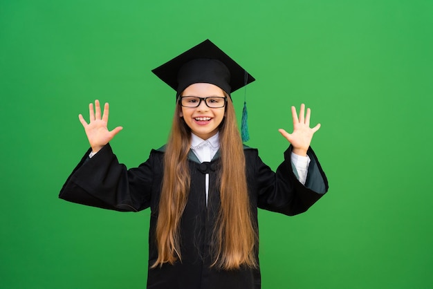 Una bella ragazza carina in uniforme scolastica, molto felice di ricevere un'istruzione a scuola, esami alla fine dell'anno scolastico, una studentessa in abito e berretto da maestro, una ragazza su uno sfondo verde isolato