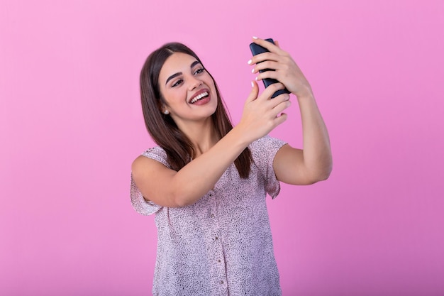 Cute beautiful girl with long hair in studio with pink walls making a selfie She looks at her smartphone and makes a selfie