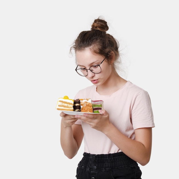 Cute beautiful happy teen girl with glasses holds cream cake in hand on white background