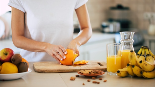 Cute beautiful and happy young brunette woman in the kitchen at home is preparing orange juice