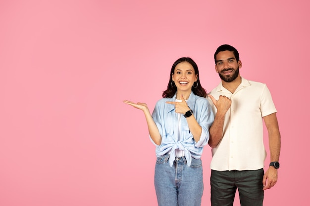 Photo cute beautiful hispanic couple pointing at copy space on pink