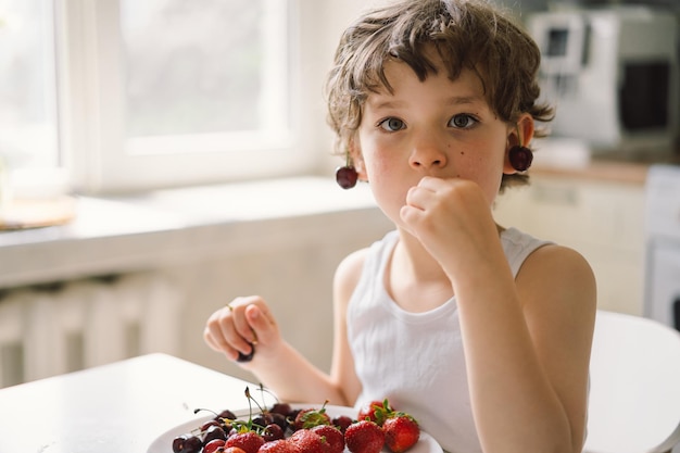 新鮮なチェリーとイチゴを食べるかわいい美しい男の子 健康食品の子供時代と開発