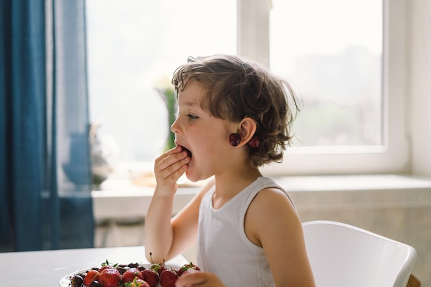 신선한 체리와 딸기를 먹는 귀여운 아름다운 소년 건강 식품 어린 시절과 발달