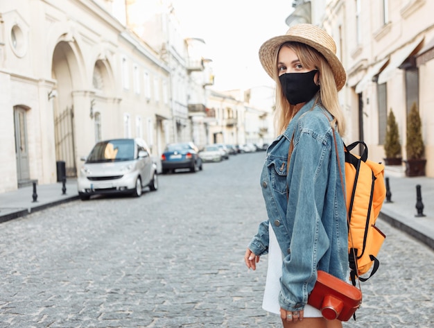 Cute beautiful millennial tourist woman with backpack in madicine face mask discover European city during the covid-19 pandemic at holiday travel.