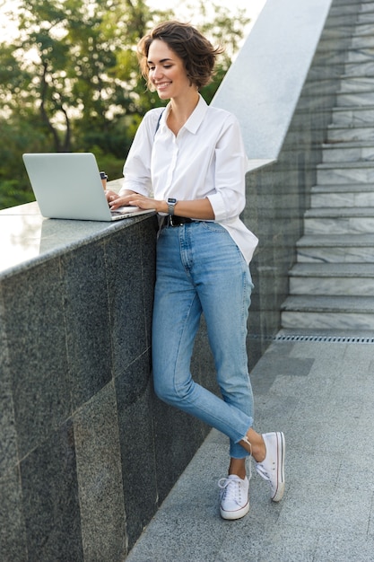 Cute beautiful woman walking outdoors using laptop computer