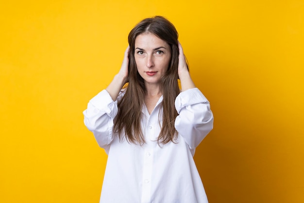 Cute beautiful young woman in a white shirt on a yellow background