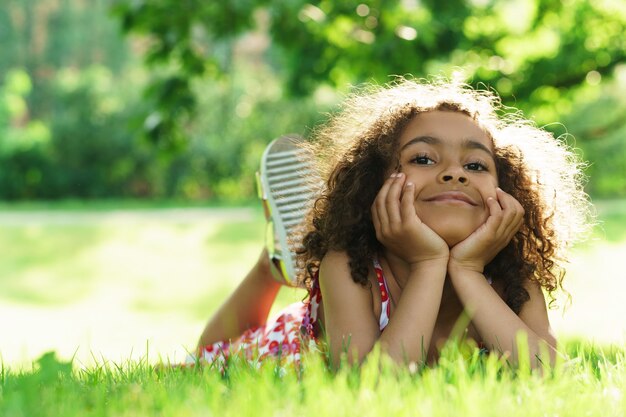 Cute black girl lying on a grass in a city park