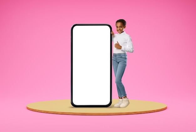 Cute black girl standing near big blank smartphone with white screen