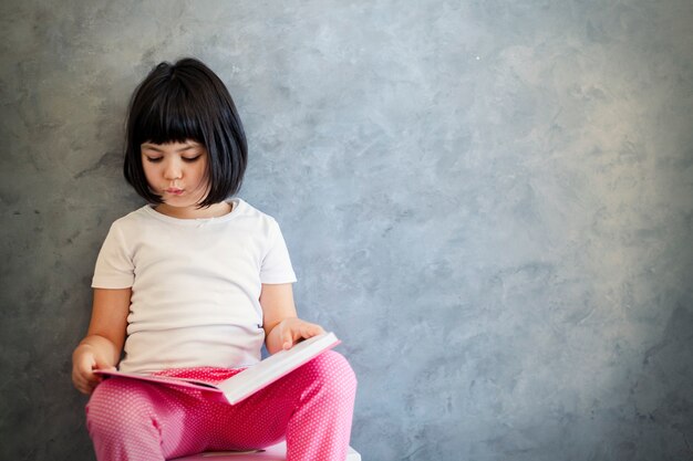 Cute black hair little girl reading book by the wall