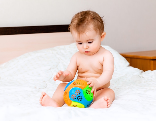 Cute blond baby playing with a ball sitting on the bed in the bedroom. happy baby 6 months old playing with a ball