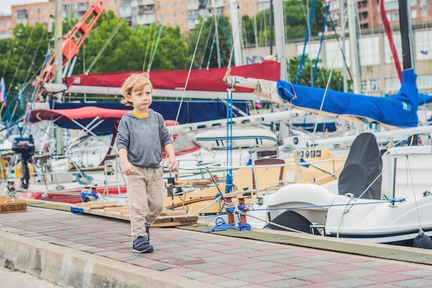 Милый белокурый мальчик, глядя на яхты и парусники