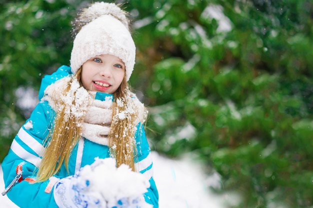 手に雪玉を持つかわいいブロンドの女の子が笑っています