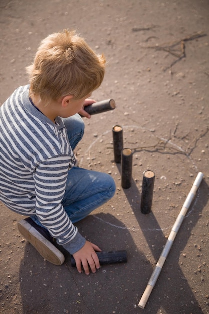 Cute blond kid boy in a striped sweatshit playing skittles in the street Russian game