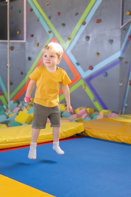 Cute blond little boy jumps in a trampoline park children activity