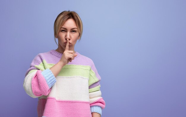 Photo cute blond woman in casual striped sweater asking to be quiet covering her mouth with finger on