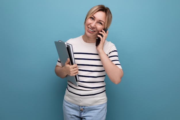 Donna bionda carina che parla al telefono con in mano un computer portatile su sfondo blu con copia