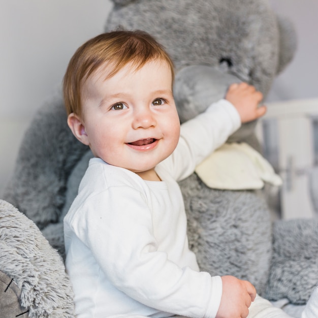 Cute blonde baby in white bed with teddy bear