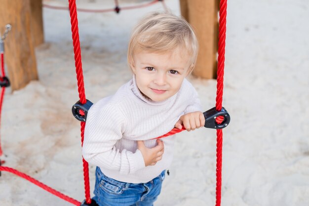 cute blonde boy climbs a rope ladder in the fresh air