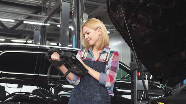 Cute blonde car mechanic engaged in car diagnostics, small business