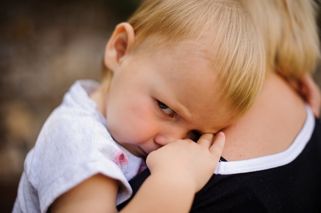 Foto bambino biondo sveglio che si trova sulla spalla della mamma