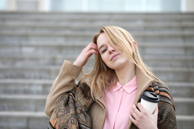 Cute blonde in the city drinking coffee on the stairs