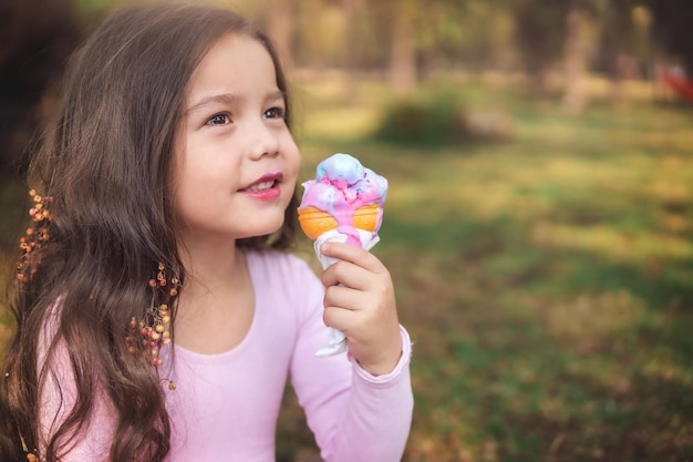 Cute blonde curlyhaired girl eating a nice ice cream in the park concept of children39s day