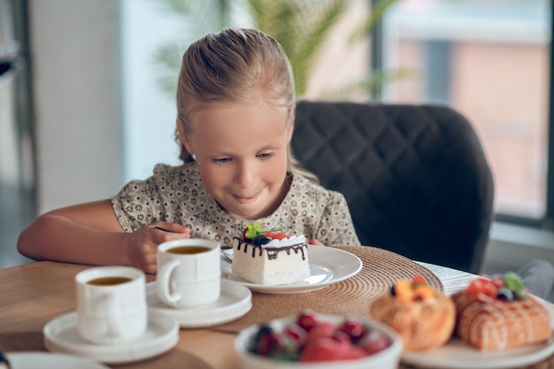 Foto una ragazza bionda carina che sembra anticipata mentre guarda la fetta di torta