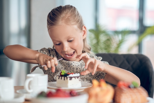 ケーキのスライスを見ながら期待して見えるかわいいブロンドの女の子