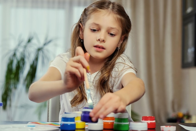 Cute blonde girl painting with acrylic paint in art studio class.