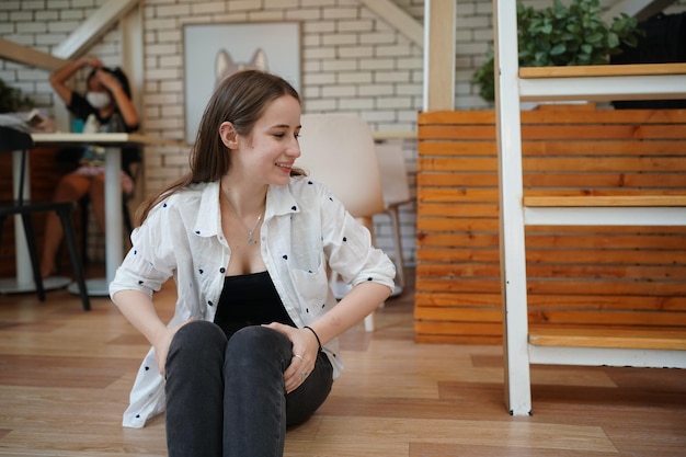 Foto ragazza bionda sveglia che si siede sul pavimento e che distoglie lo sguardo