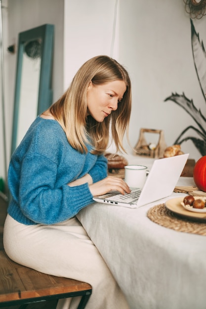 Foto ragazza bionda carina che lavora la mattina su un computer portatile e bere caffè