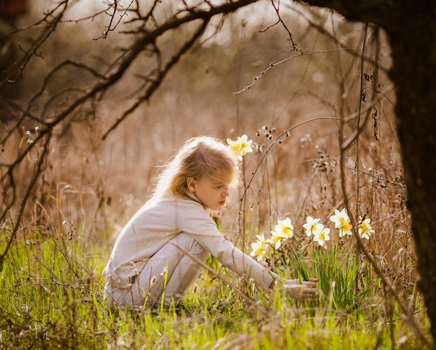 Cute blonde happy little girl with yellow daffodils in the spring country