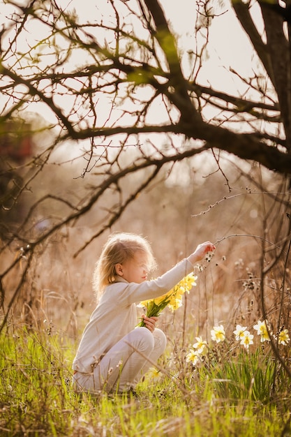 Cute blonde happy little girl with yellow daffodils in the spring country